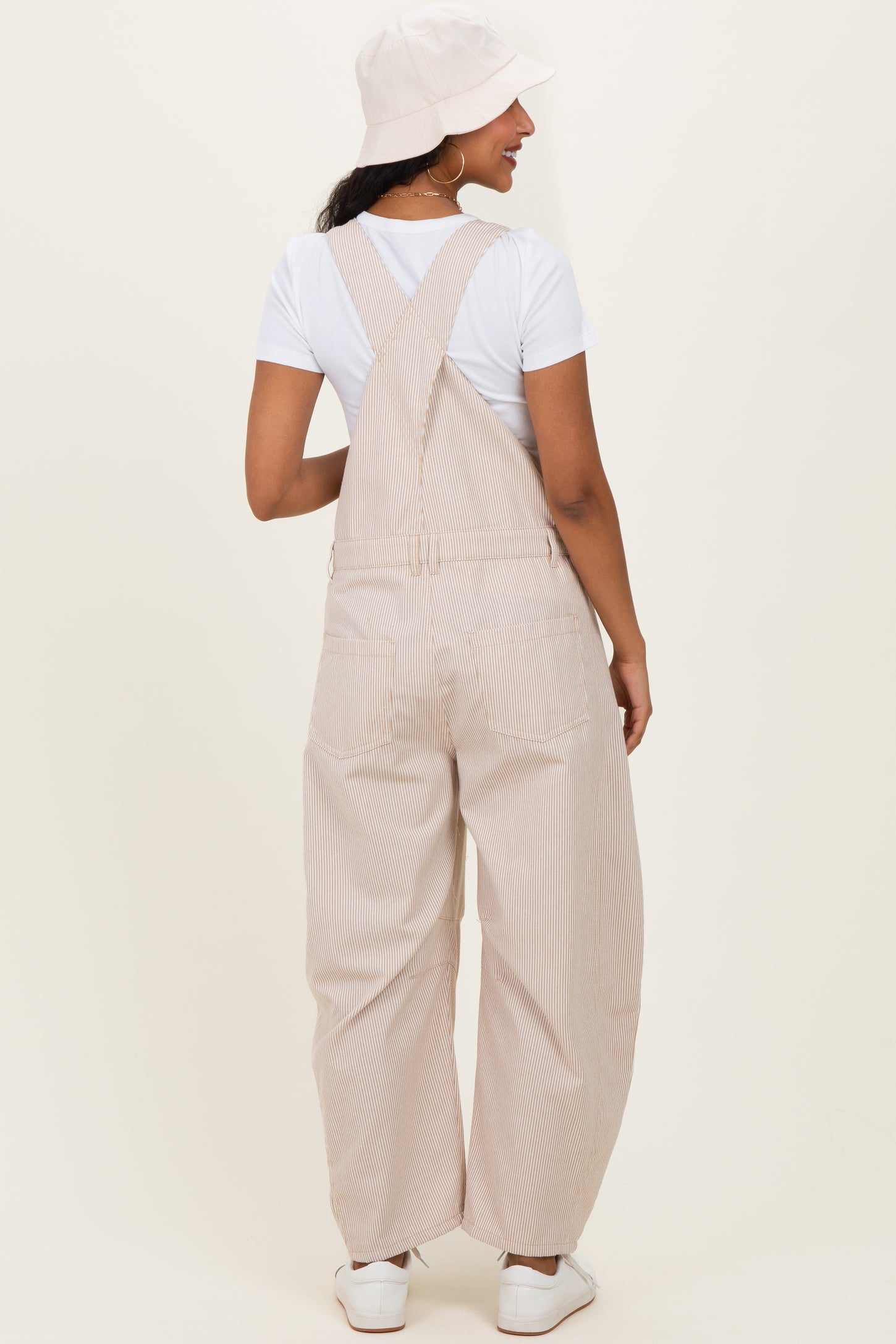 woman wearing a striped beige maternity overall with a white t-shirt and a bucket hat, showing her back