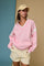 woman wearing a pink oversized v-neck sweatshirt with white stripes and cream-colored shorts, accessorized with a beige cap