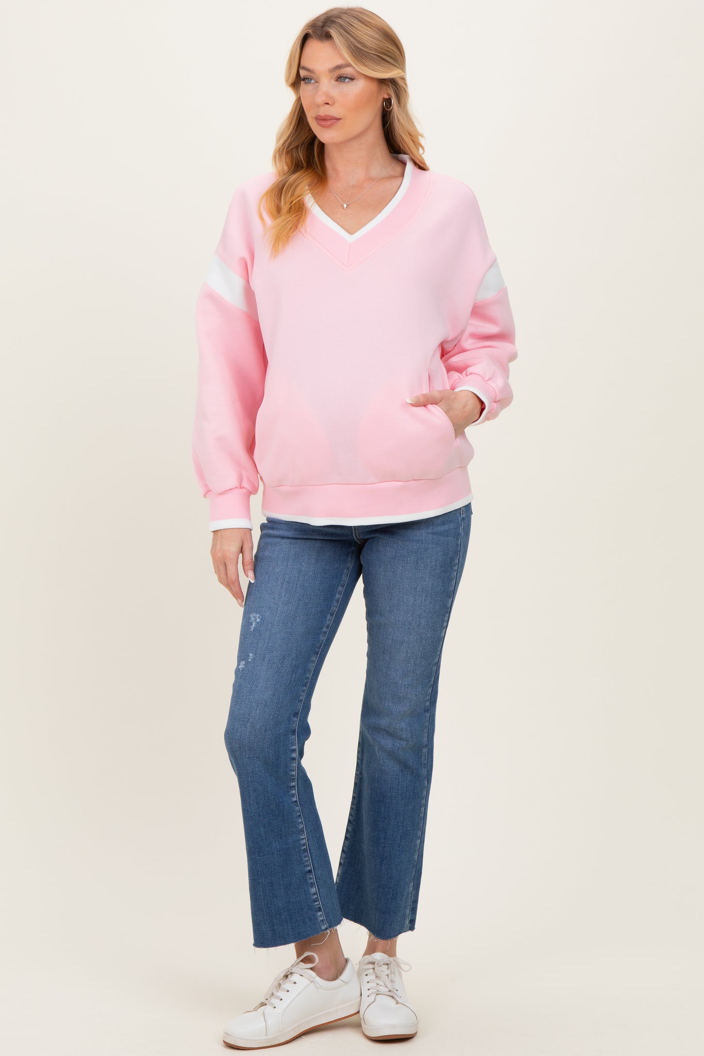 woman wearing a pink maternity sweatshirt with a v-neck and long sleeves, paired with flared jeans and white sneakers