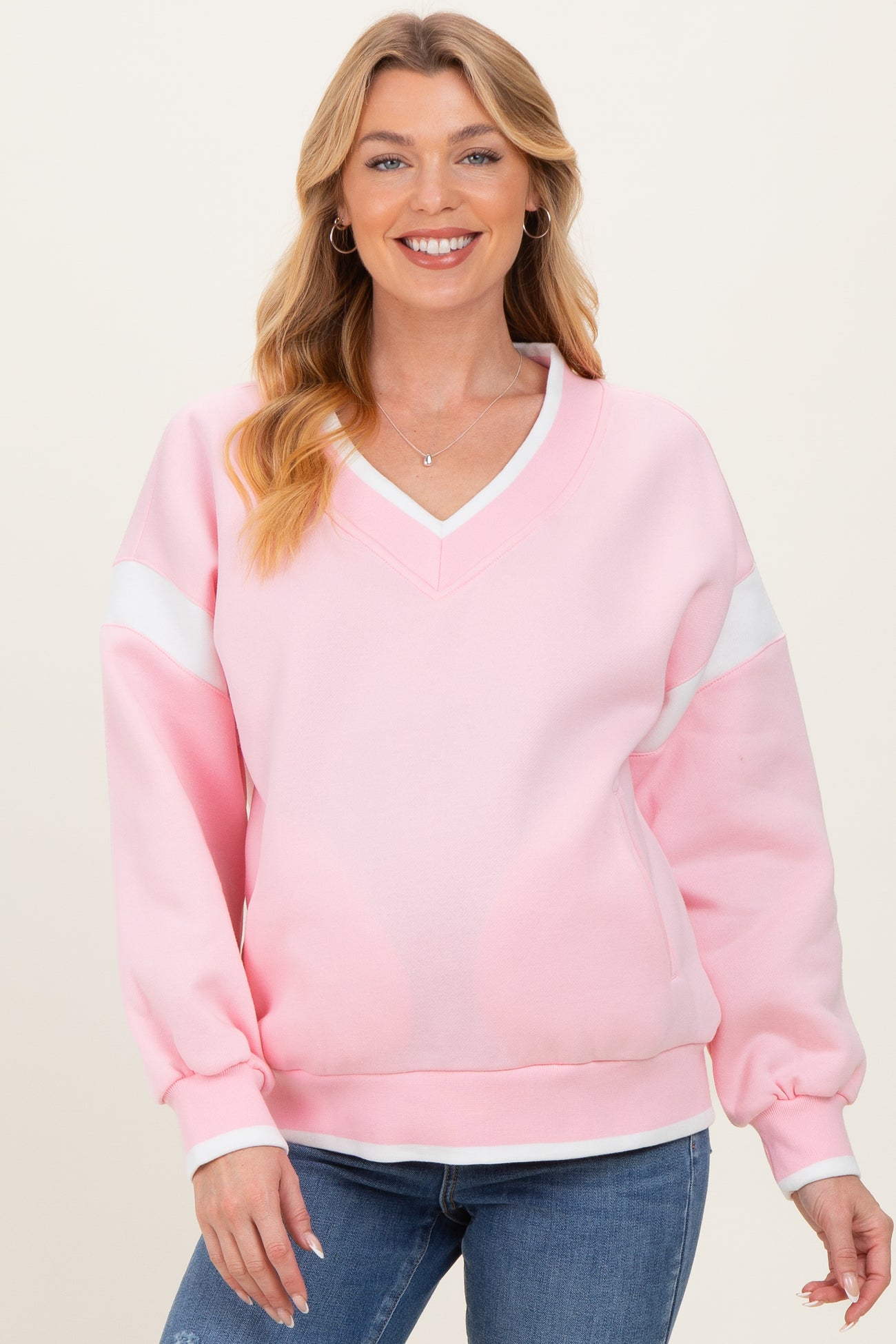 woman wearing a light pink v-neck maternity sweatshirt with white accents, smiling at the camera