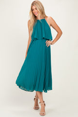 woman wearing a teal sleeveless pleated maxi dress with layered top and strappy heels