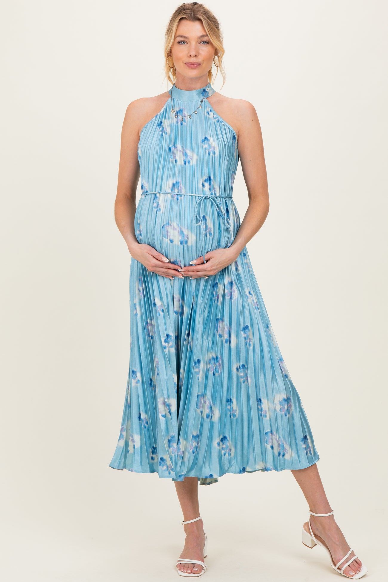 woman wearing a light blue floral pleated maternity dress with a halter neck and holding her baby bump