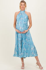 woman wearing a light blue floral pleated maternity dress with a halter neck and holding her baby bump