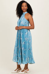 woman wearing a blue pleated midi dress with floral patterns and a halter neck, styled with white flats