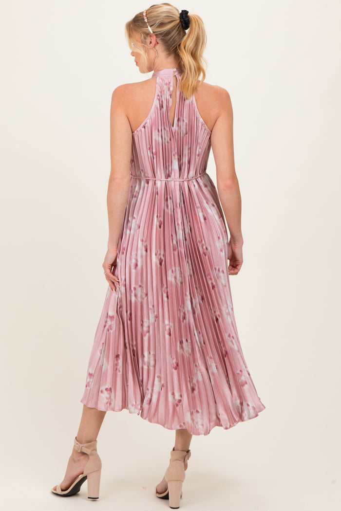 woman wearing a pink floral pleated maternity dress with a halter neckline and a flowing midi skirt