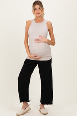 woman wearing a light beige maternity tank top and black wide-leg pants, holding her baby bump