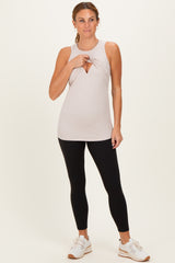 woman wearing a taupe sleeveless workout top with a cutout detail and black leggings, standing in a relaxed pose