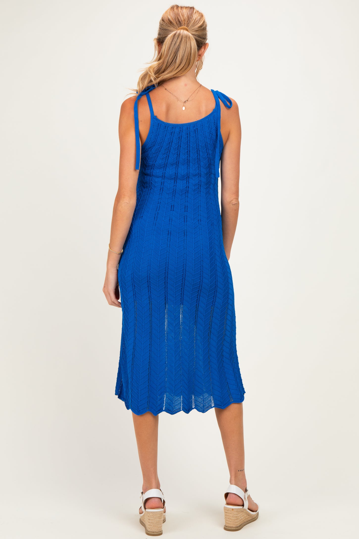 woman wearing a blue knitted maternity dress with adjustable tie straps and a mid-length hemline