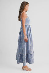 woman wearing a light blue maxi dress with floral embroidery and a tiered hem, styled with strappy sandals