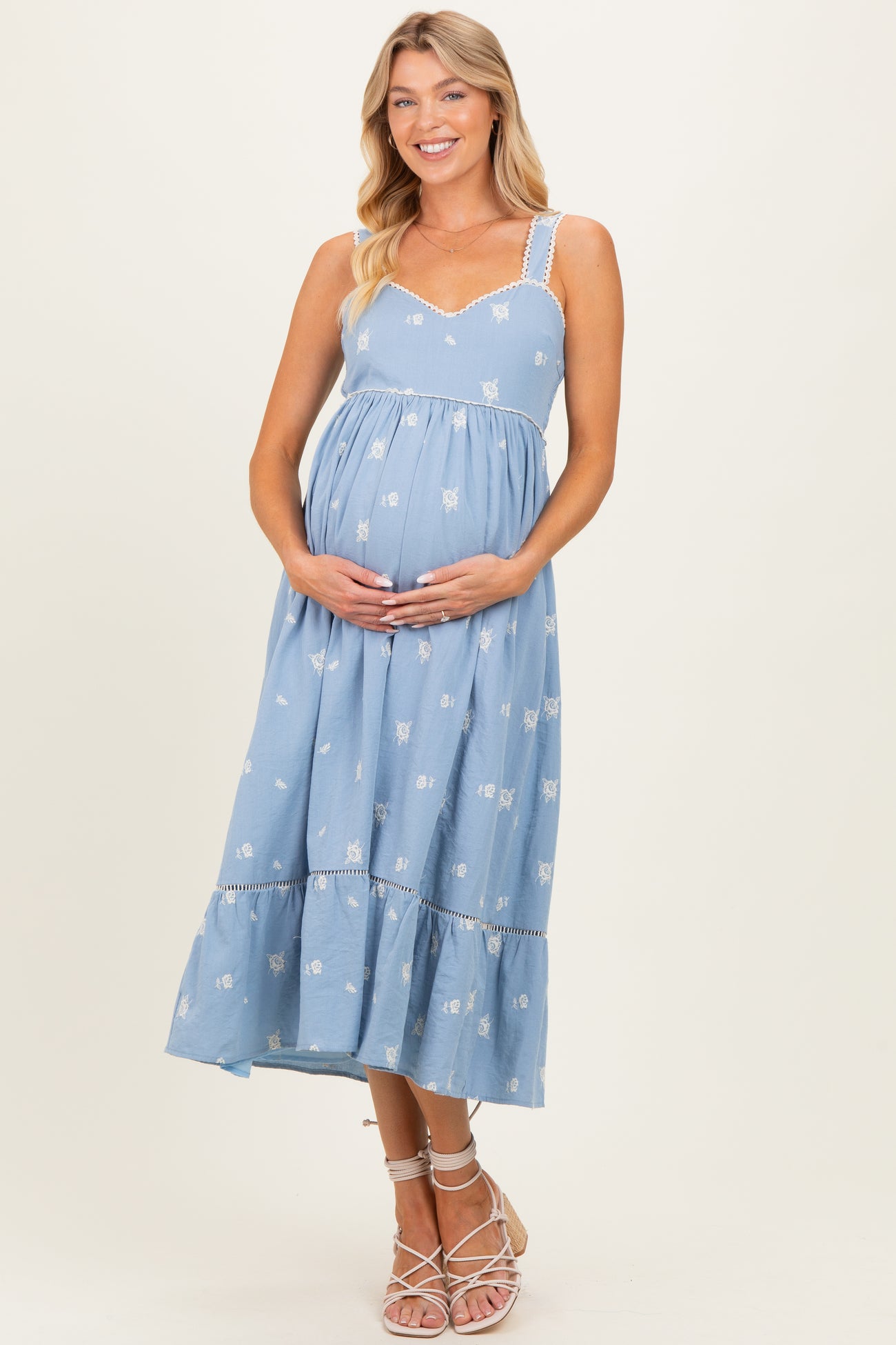 woman wearing a light blue maternity dress with floral print and spaghetti straps, gently holding her baby bump