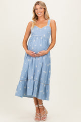 woman wearing a light blue maternity dress with floral print and spaghetti straps, gently holding her baby bump