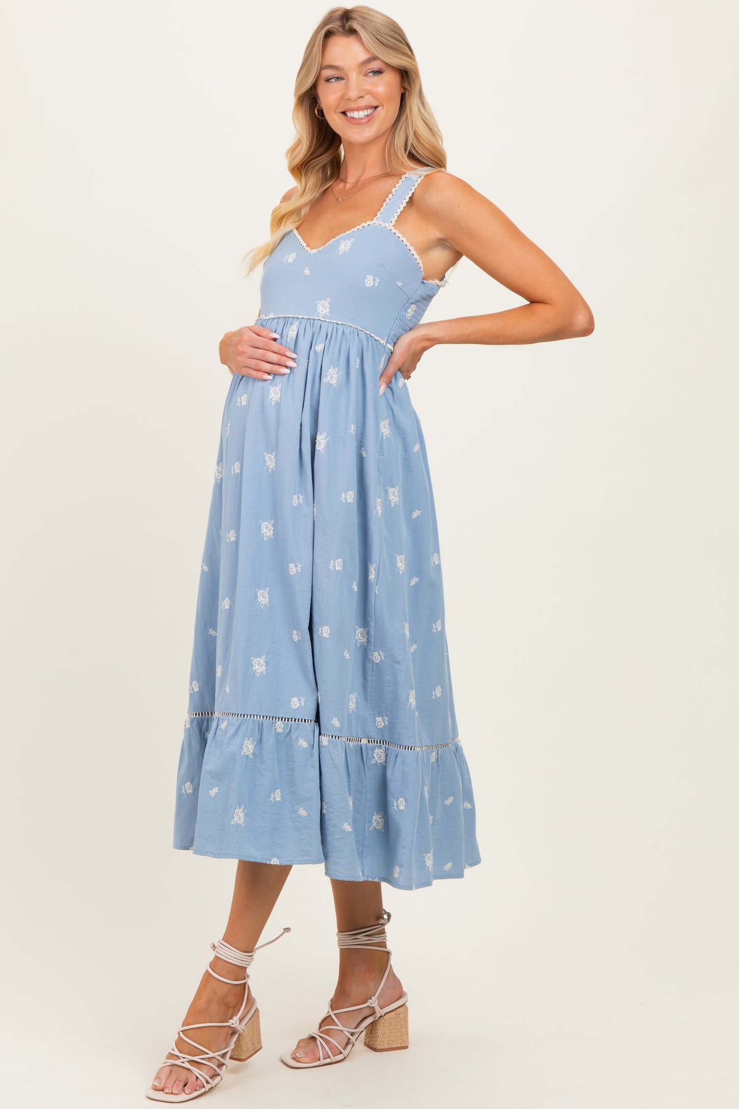woman wearing a light blue maternity dress with floral embroidery and a tiered hem, showing her baby bump