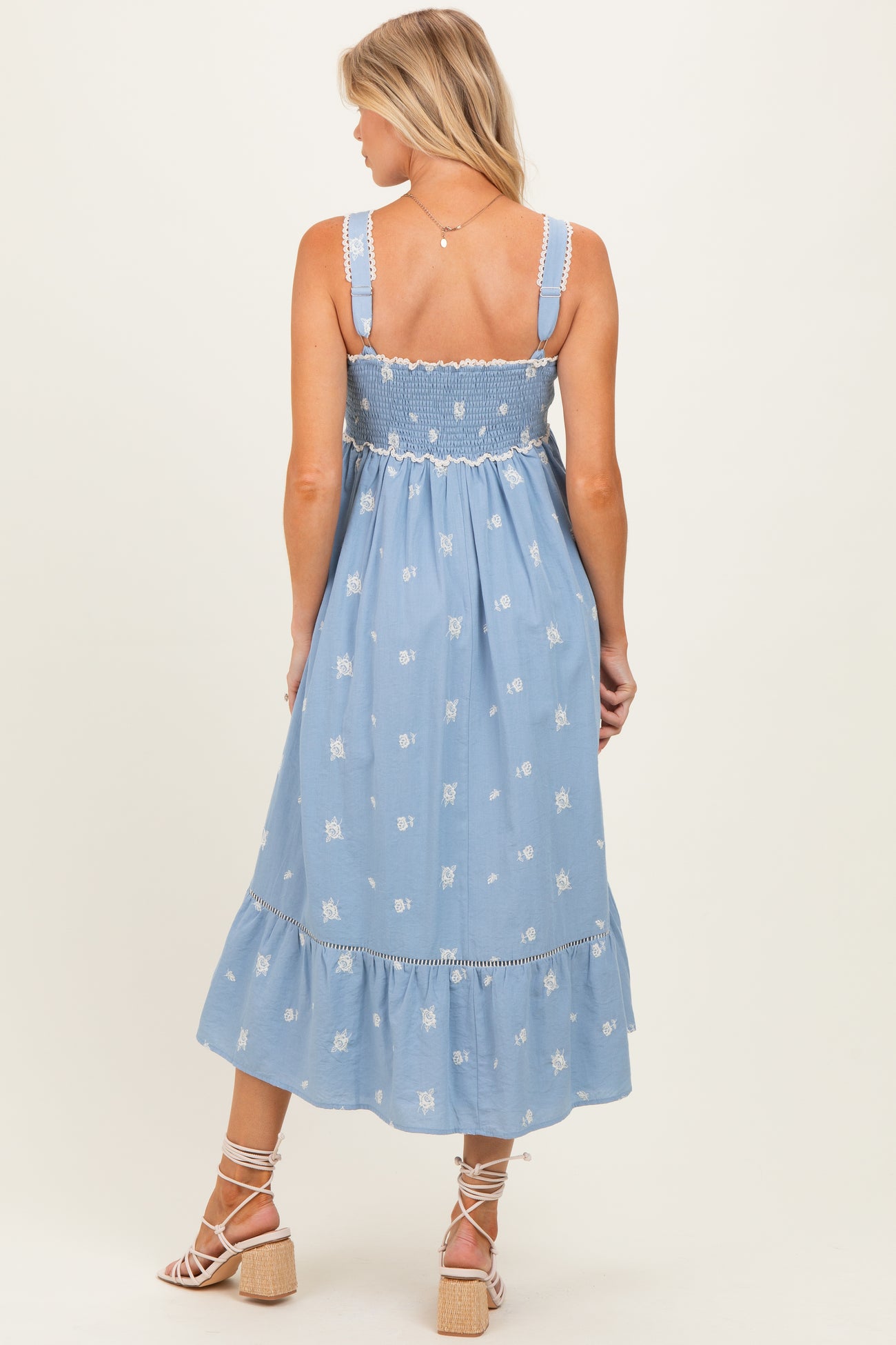 woman wearing a blue embroidered maternity dress with a smocked bodice and tiered hem, showing her baby bump
