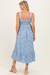 woman wearing a blue embroidered maternity dress with a smocked bodice and tiered hem, showing her baby bump