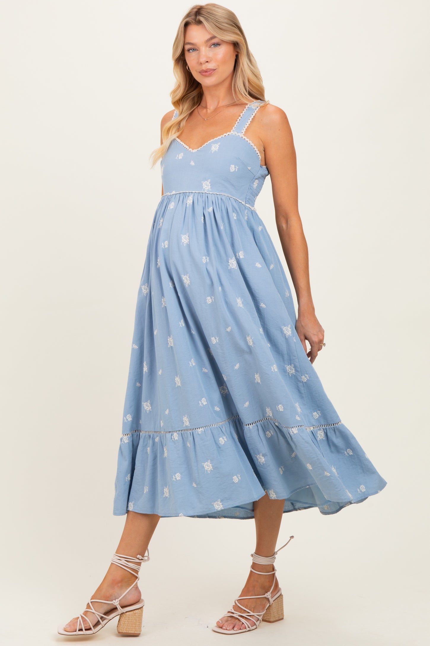 woman wearing a light blue maternity dress with embroidered flowers and ruffled hem, showcasing her baby bump