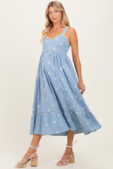 woman wearing a light blue maternity dress with embroidered flowers and ruffled hem, showcasing her baby bump