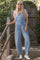 woman wearing a striped t-shirt and light blue denim overalls with relaxed fit and white sneakers, standing outdoors