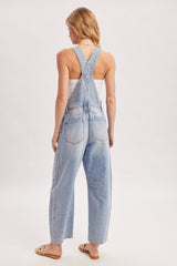 woman wearing light blue denim overalls with a loose fit and adjustable straps, seen from the back