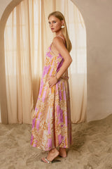 woman wearing a pink and cream floral maxi dress with spaghetti straps, standing against a soft beige backdrop