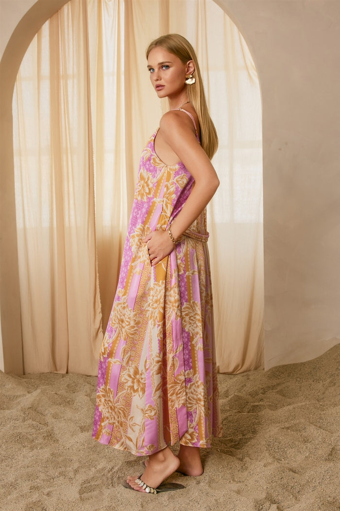 woman wearing a pink and cream floral maxi dress with spaghetti straps, standing against a soft beige backdrop