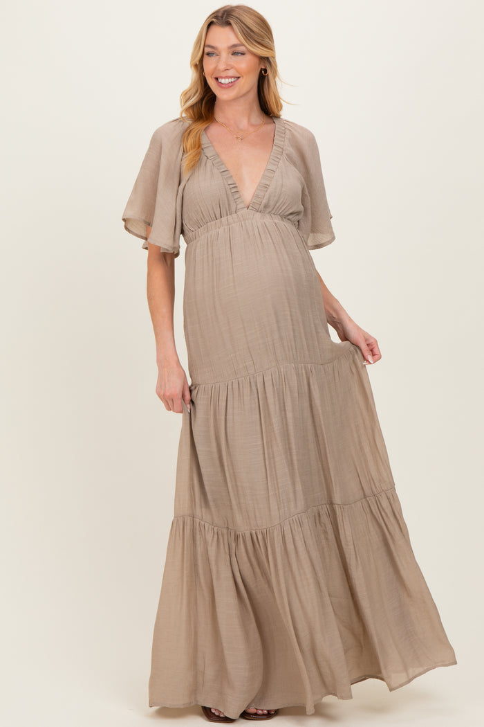 woman wearing a beige v-neck maxi maternity dress with flutter sleeves and tiered skirt, showing her baby bump