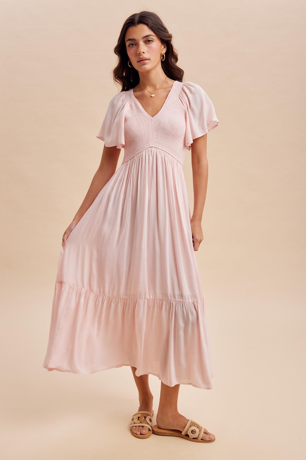 woman wearing a light pink flowy maxi dress with short puff sleeves and a tiered skirt