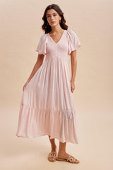 woman wearing a light pink flowy maxi dress with short puff sleeves and a tiered skirt