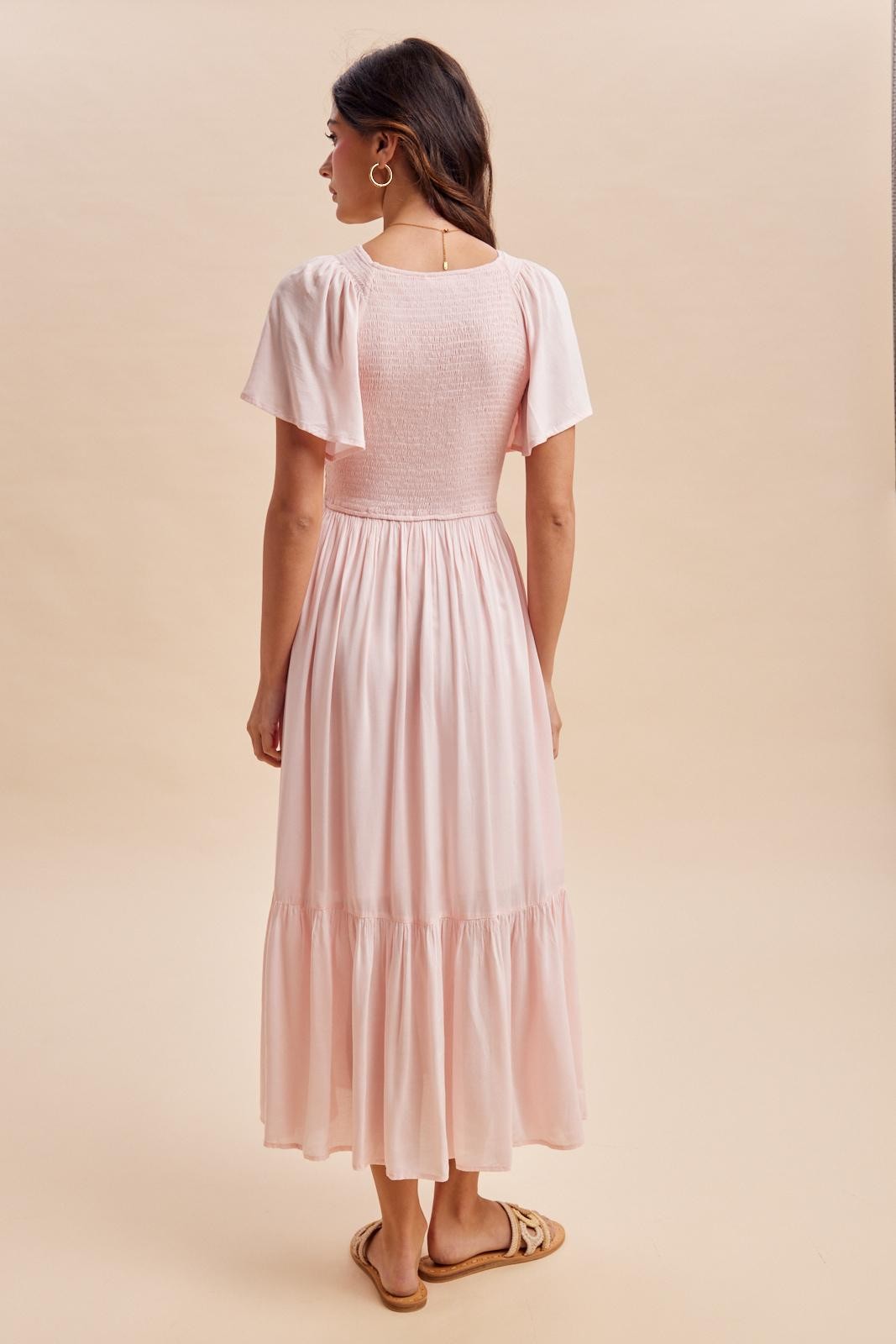 woman wearing a light pink maxi dress with short sleeves and a smocked bodice, viewed from the back
