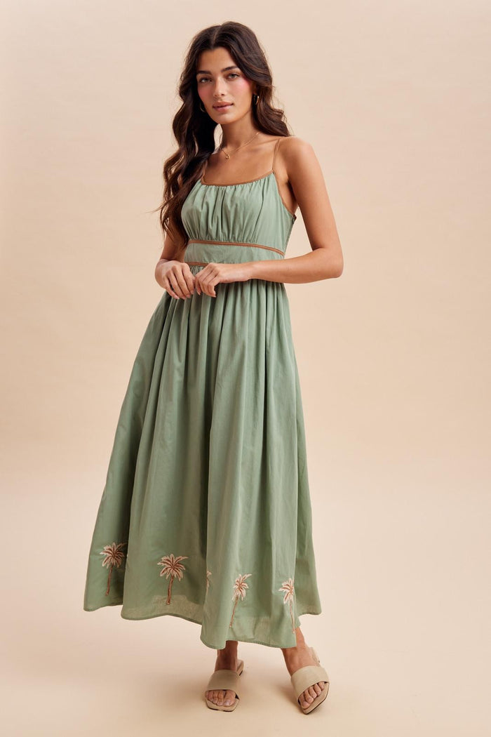 woman wearing a green strapless maxi dress with embroidery at the hem and a fitted bodice