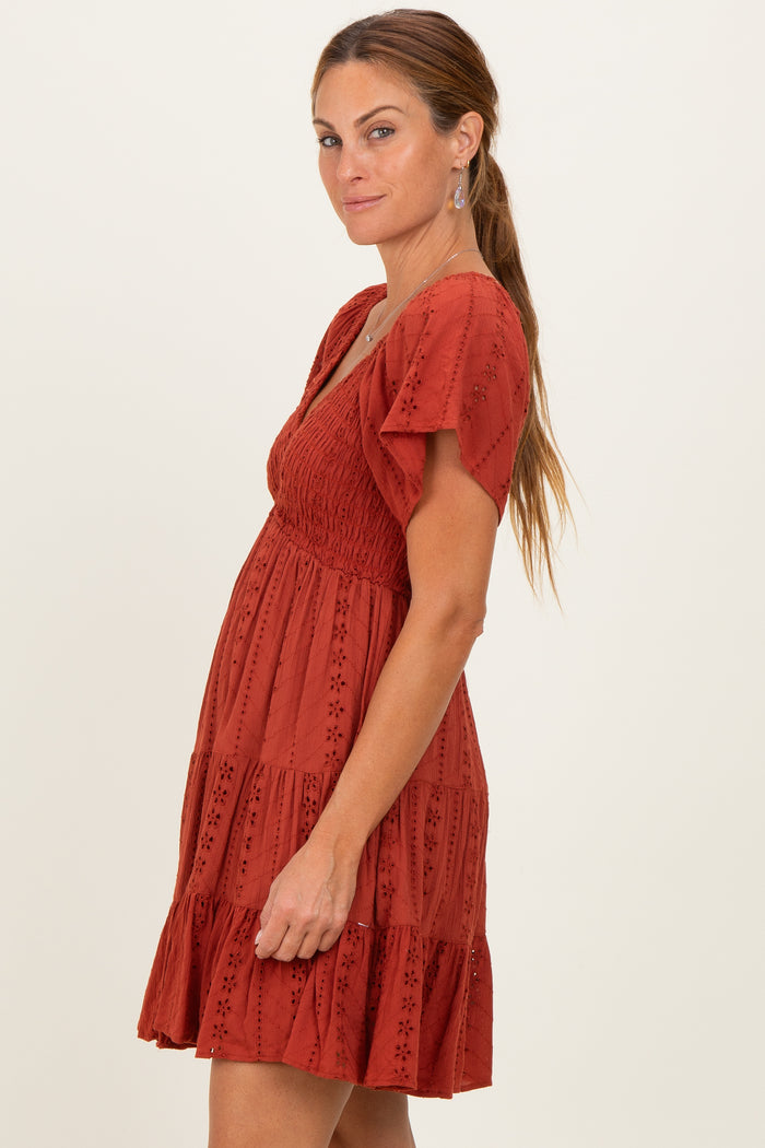 woman wearing a rust-colored short sleeve dress with a smocked bodice and tiered skirt, posing sideways