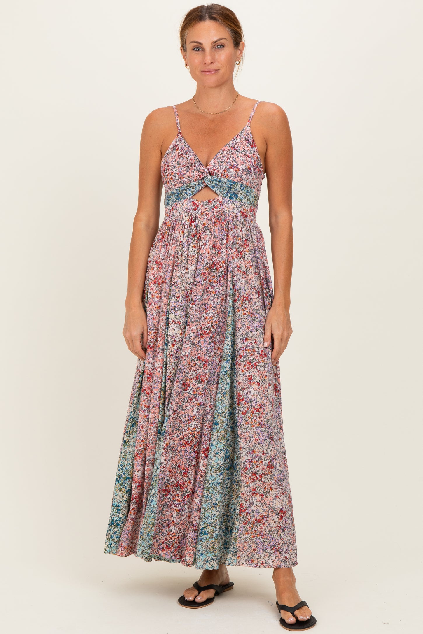 woman wearing a floral maxi dress with a cutout under the bust and spaghetti straps, standing in flip-flops