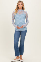 woman wearing a light blue lace maternity top and holding her baby bump, paired with distressed jeans and white slip-on shoes