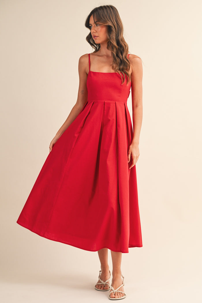 woman wearing a red sleeveless midi dress with a square neckline and pleated skirt, standing against a neutral background