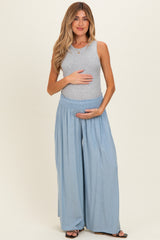 woman wearing a gray sleeveless top and light blue maternity wide-leg pants, holding her baby bump
