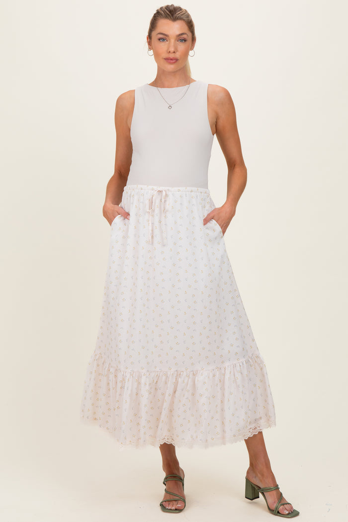 woman wearing a white floral maternity maxi skirt with pockets and a ruffled hem, paired with a sleeveless top