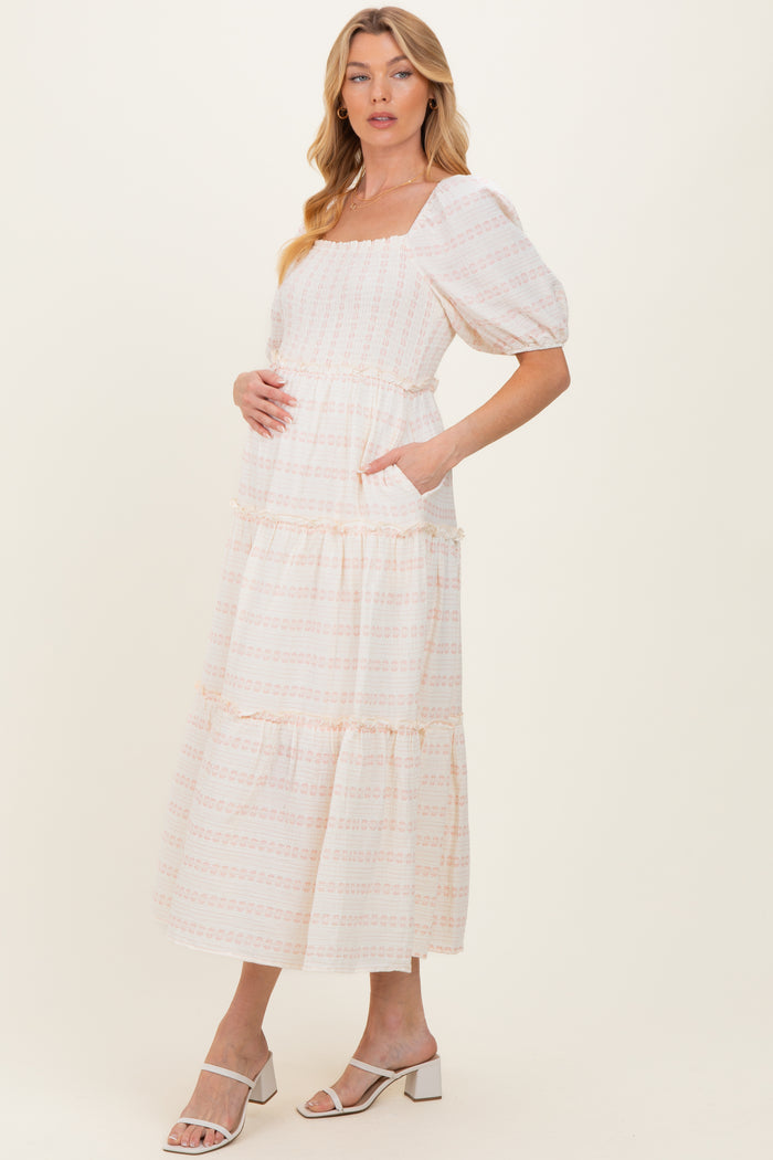 woman wearing a cream maternity maxi dress with square neckline and puff sleeves, holding her baby bump