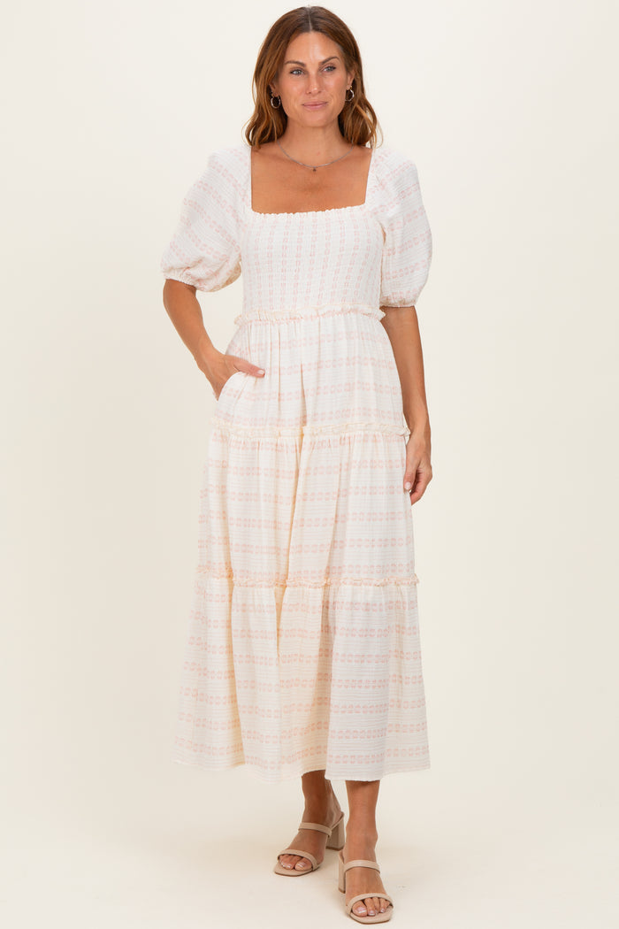 woman wearing a beige tiered maxi dress with puff sleeves and a square neckline, standing in front of a neutral background