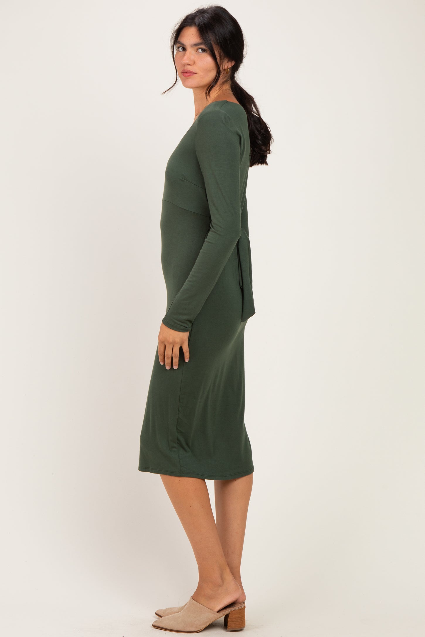 woman wearing a dark green long sleeve fitted dress with a back tie detail and a knee-length hemline