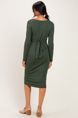 woman wearing a dark green long sleeve midi dress with a tie-back detail, standing against a neutral background
