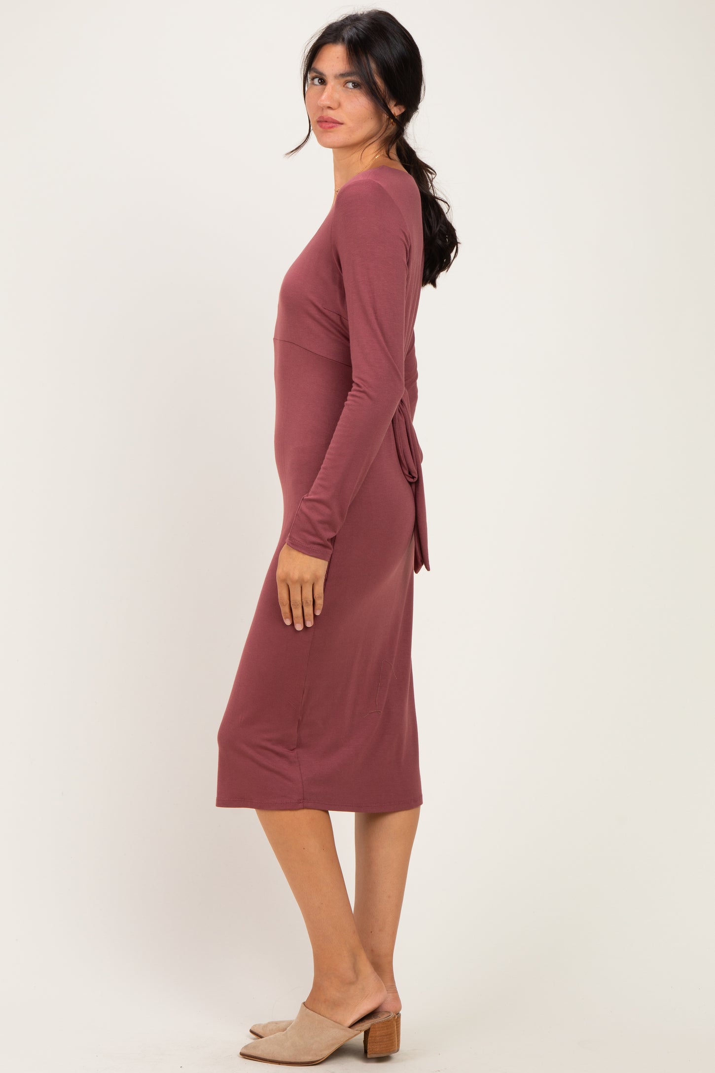 woman wearing a mauve long sleeve midi dress with a tie detail at the waist and slip-on heels