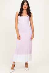 woman wearing a light pink ribbed maxi dress with white hem and decorative buttons, standing with one hand on her hip