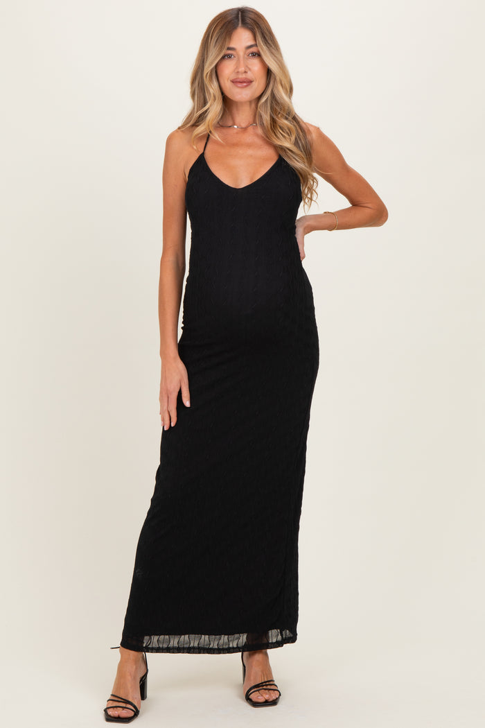 woman wearing a black maternity maxi dress with a v-neck and spaghetti straps, gently accentuating her baby bump