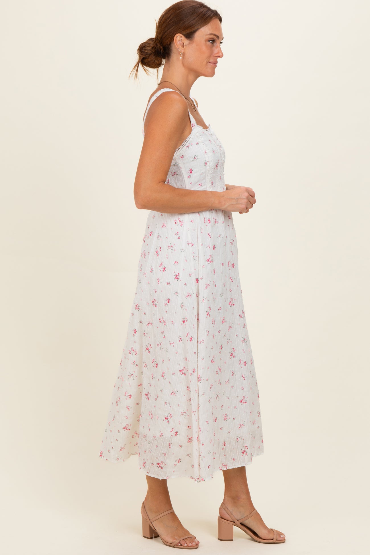 woman wearing a white midi dress with a floral pattern and spaghetti straps, standing sideways on a neutral background