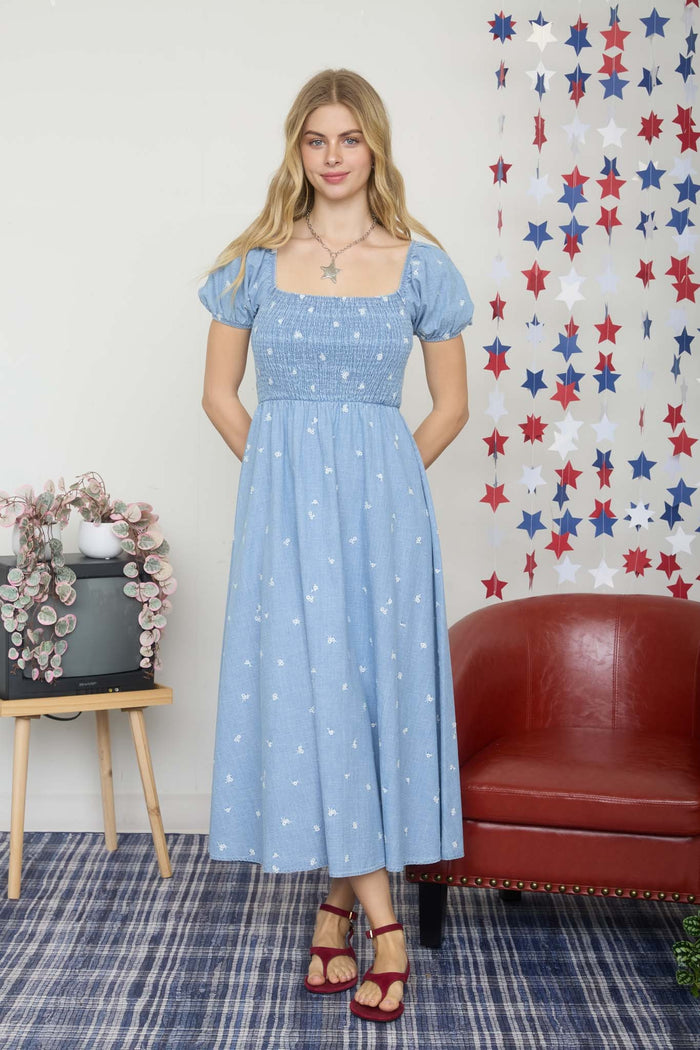 woman wearing a light blue midi dress with puff sleeves and white floral patterns, standing in a room with red and blue decor