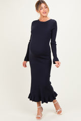 woman wearing a navy ribbed maternity dress with long sleeves and a ruffled hem, showcasing her baby bump