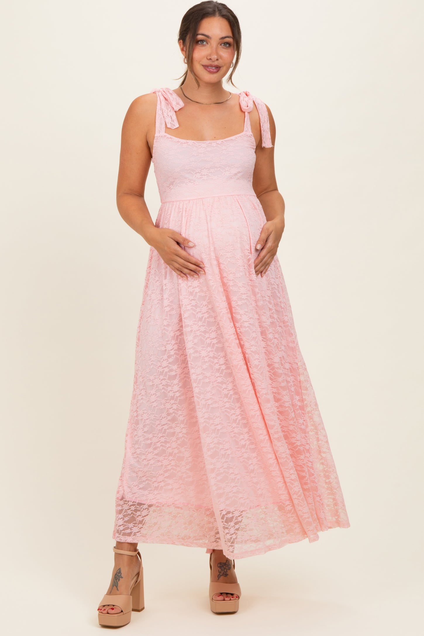 woman wearing a pink lace maternity maxi dress with tie shoulder straps and a visible baby bump