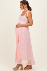 woman wearing a light pink maternity maxi dress with tie shoulder straps and holding her baby bump