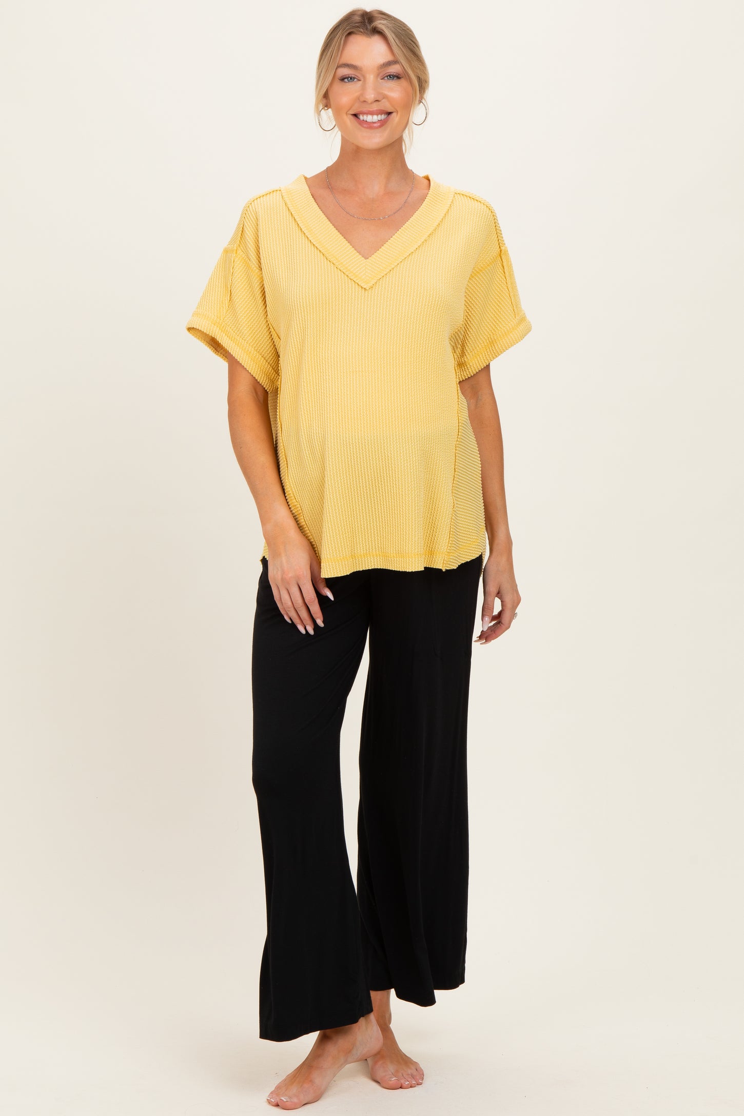 woman wearing a yellow ribbed short sleeve maternity top and black wide-leg pants, showcasing her baby bump