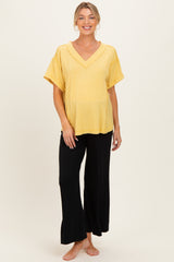 woman wearing a yellow ribbed short sleeve maternity top and black wide-leg pants, showcasing her baby bump