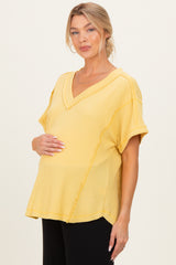 woman wearing a mustard yellow maternity top with a v-neck and short sleeves, holding her baby bump
